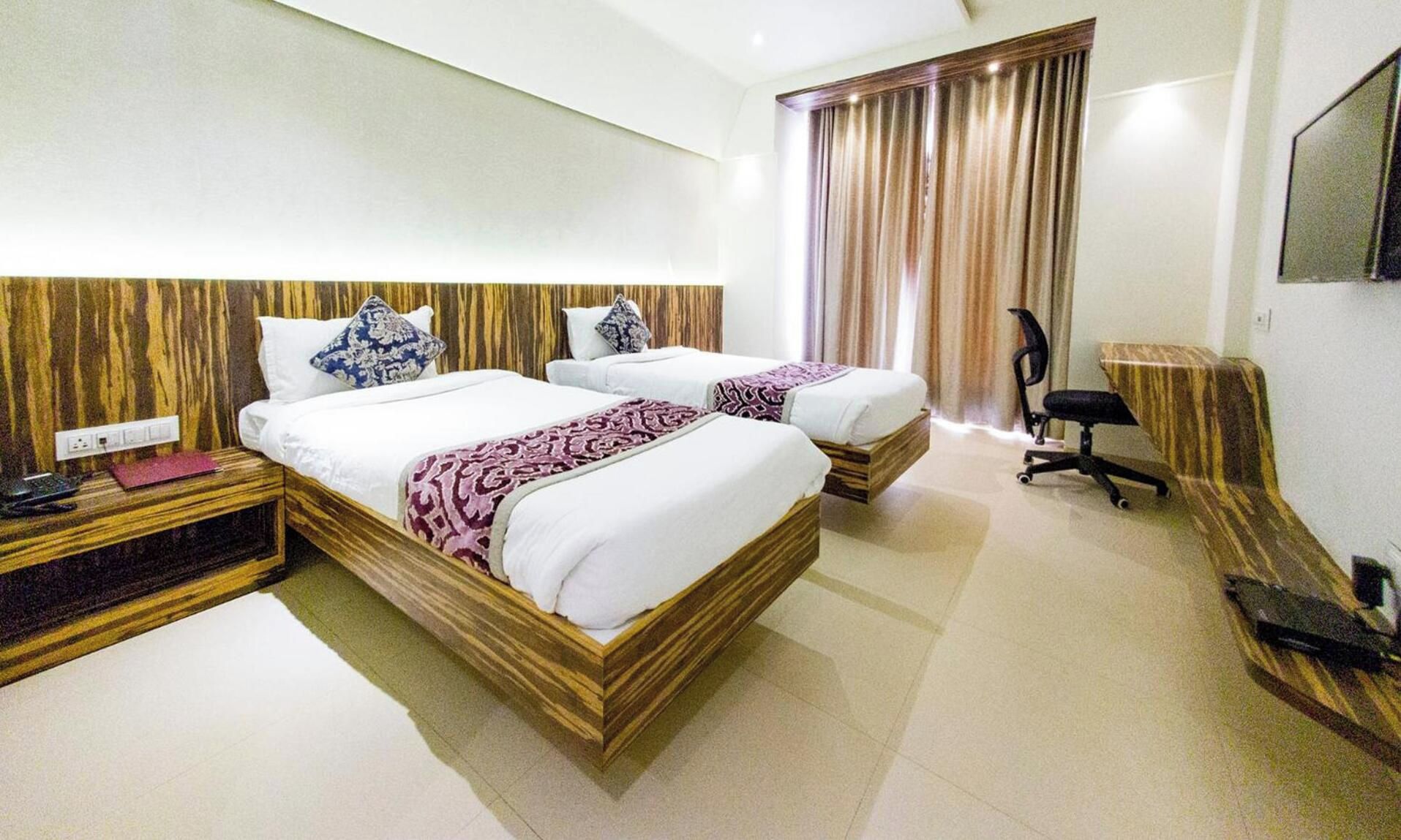 A hotel room with two beds, a desk, a chair, and a television.