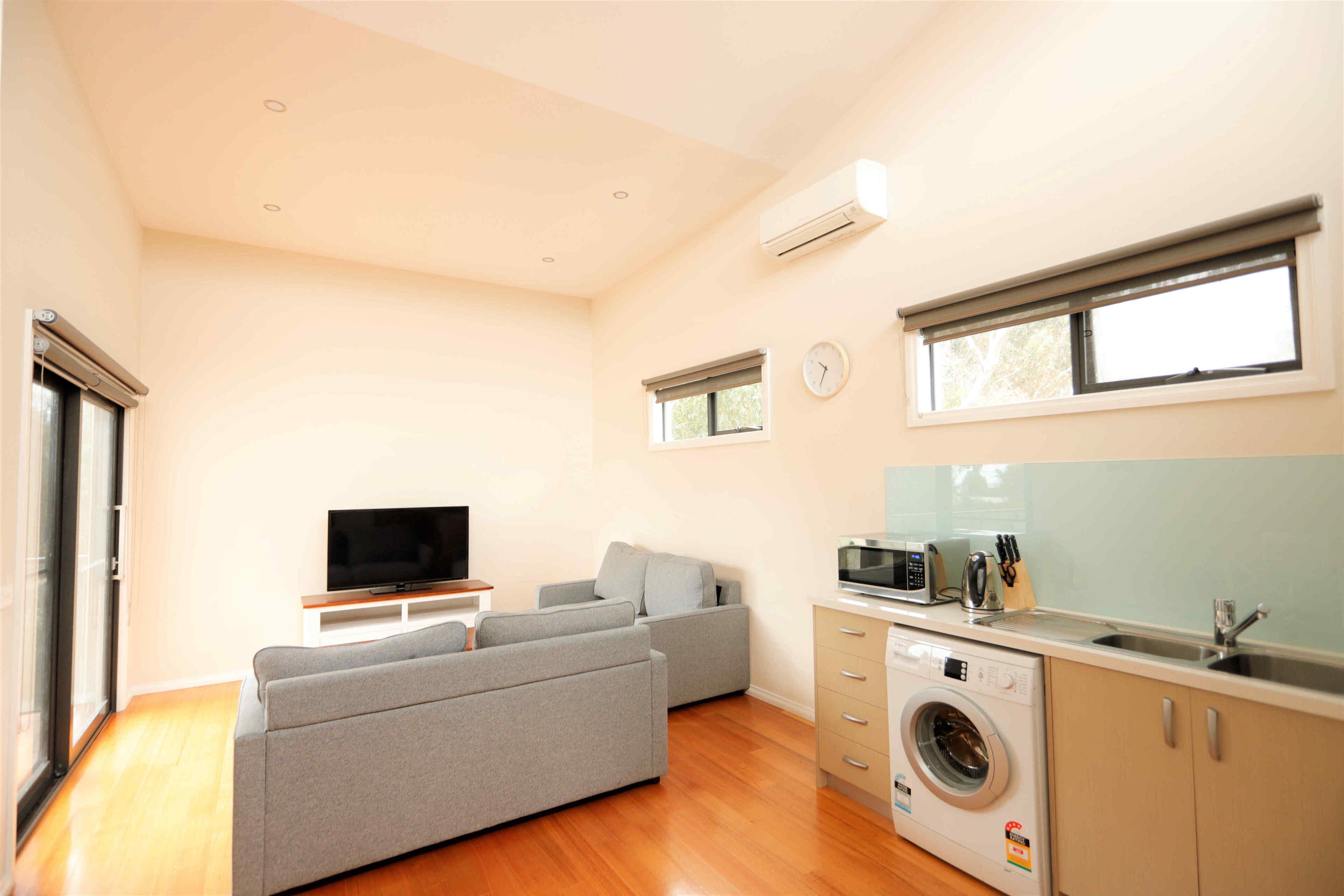 Un espace de vie compact comprenant un canapé, un téléviseur à écran plat, un lave-linge et une kitchenette.