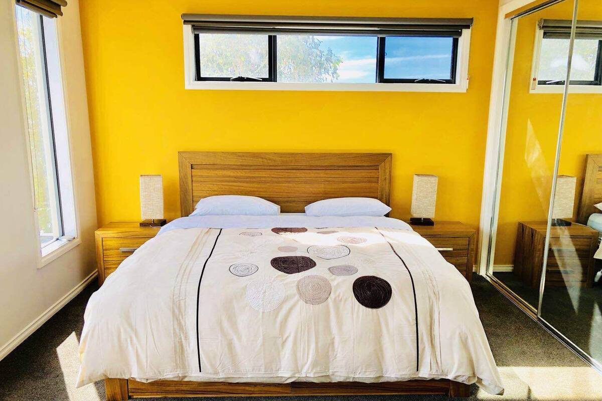 Un dormitorio con una cama, dos mesitas de noche, una ventana y un espejo.