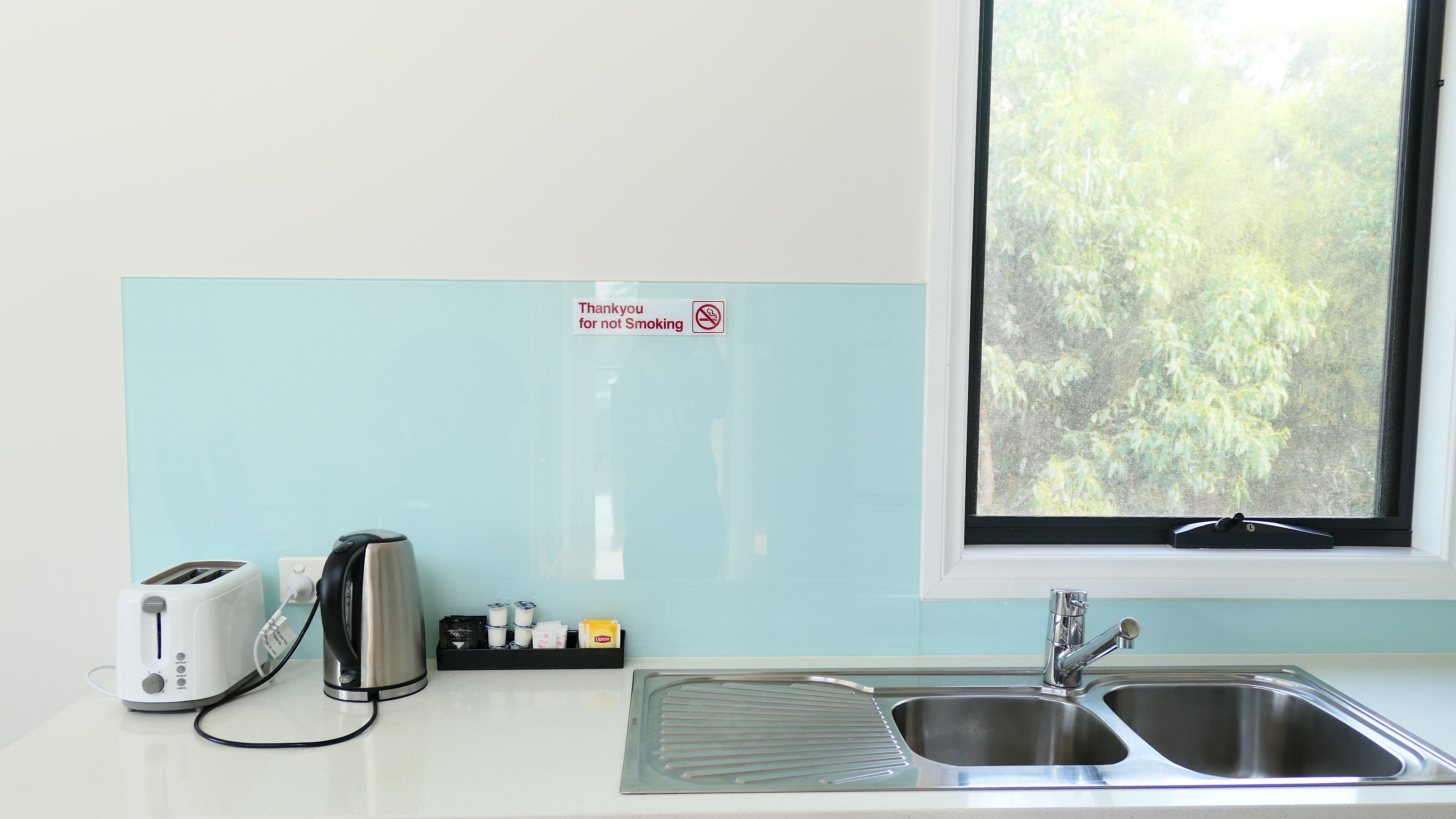A kitchen with a toaster, kettle, and a sign prohibiting smoking.