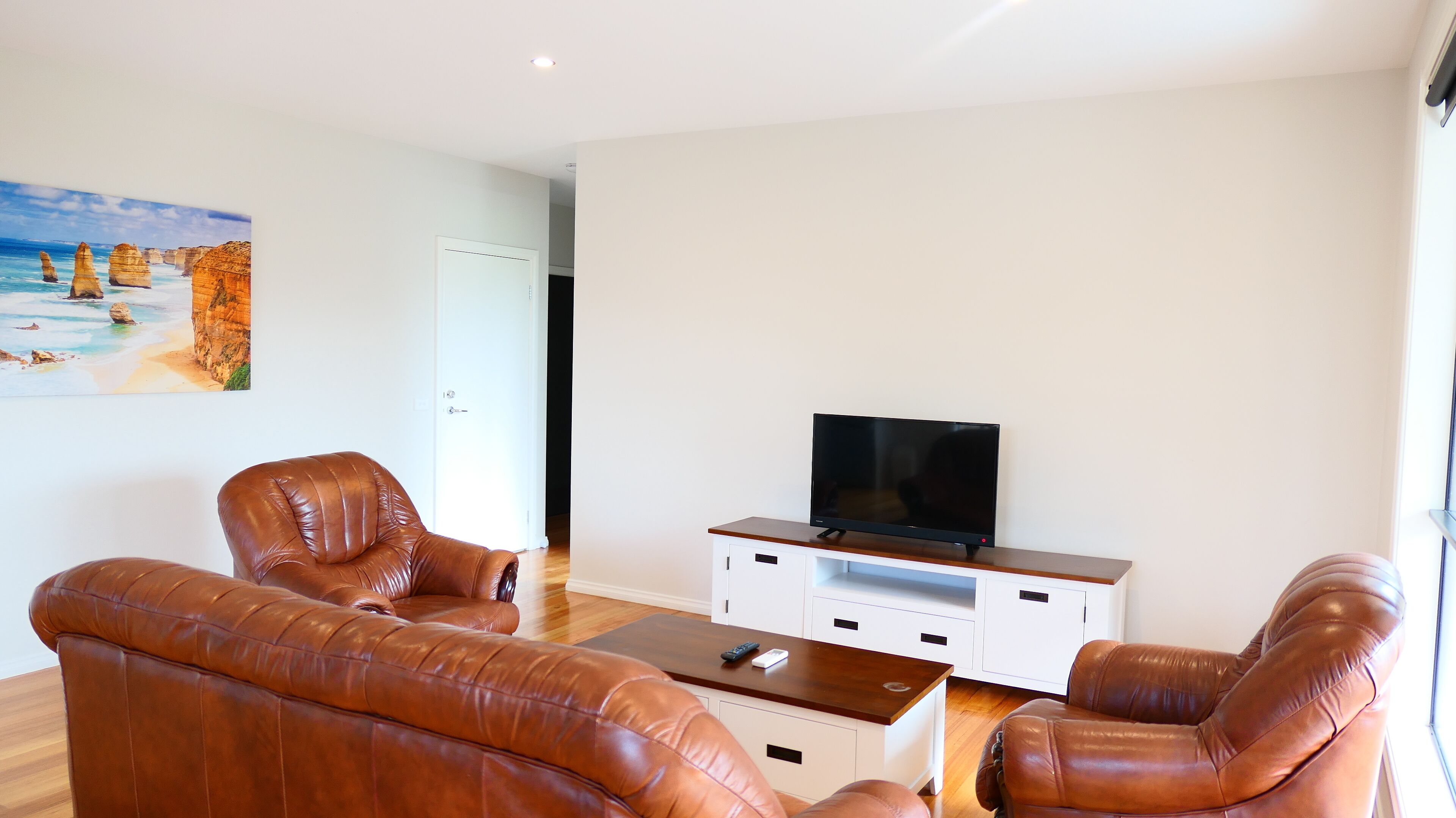 A living room with leather sofas, a coffee table, and a TV on a wooden stand.