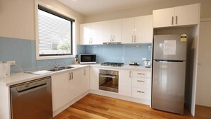 A modern kitchen with white cabinets, a stainless steel refrigerator, a microwave, a dishwasher, and a gas stove. - Apollo Bay Seal Apartments (Marengo)