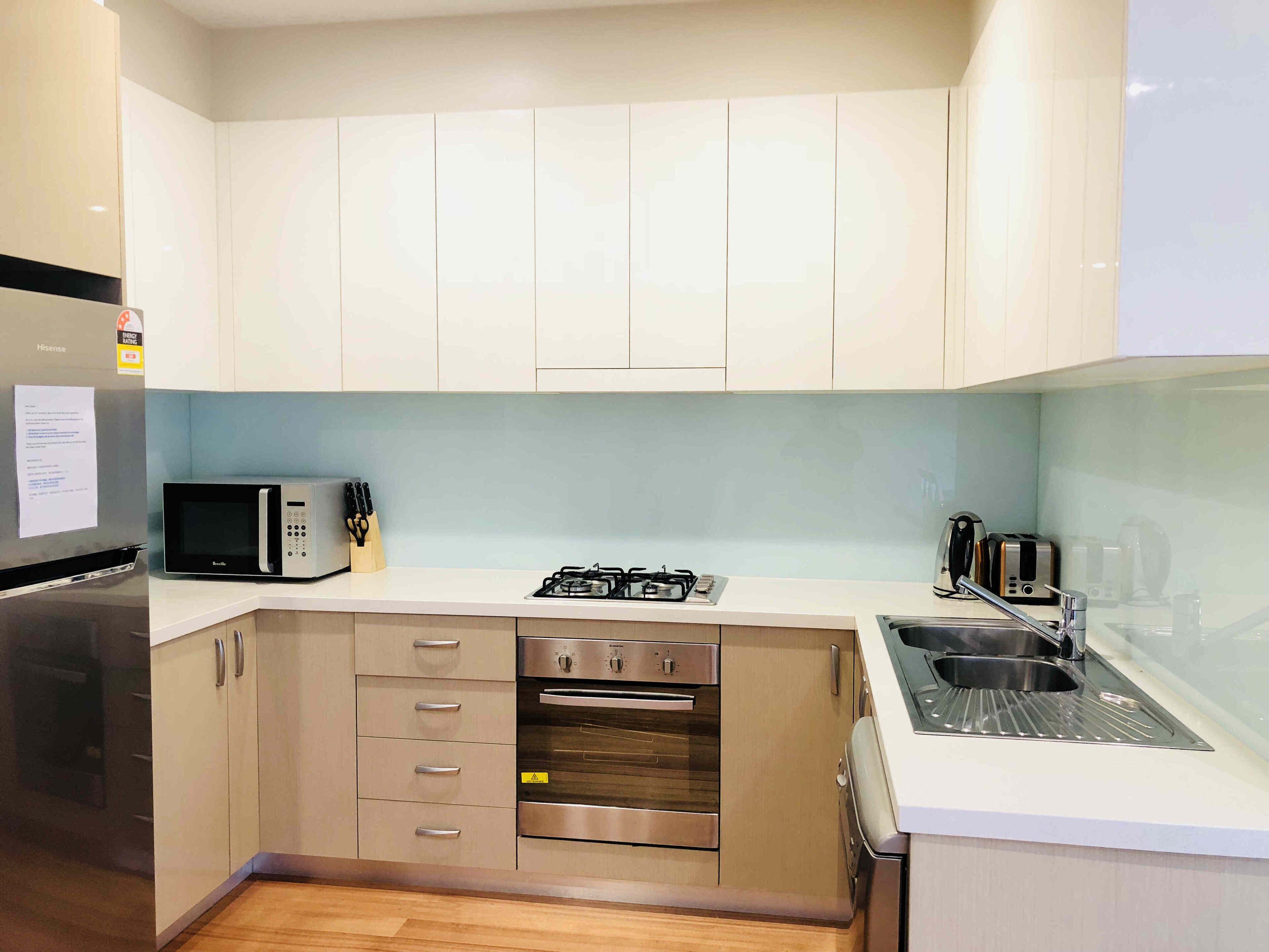 A modern kitchen with white cabinets, a stainless steel refrigerator, a microwave, a gas stove, an oven, and a sink.