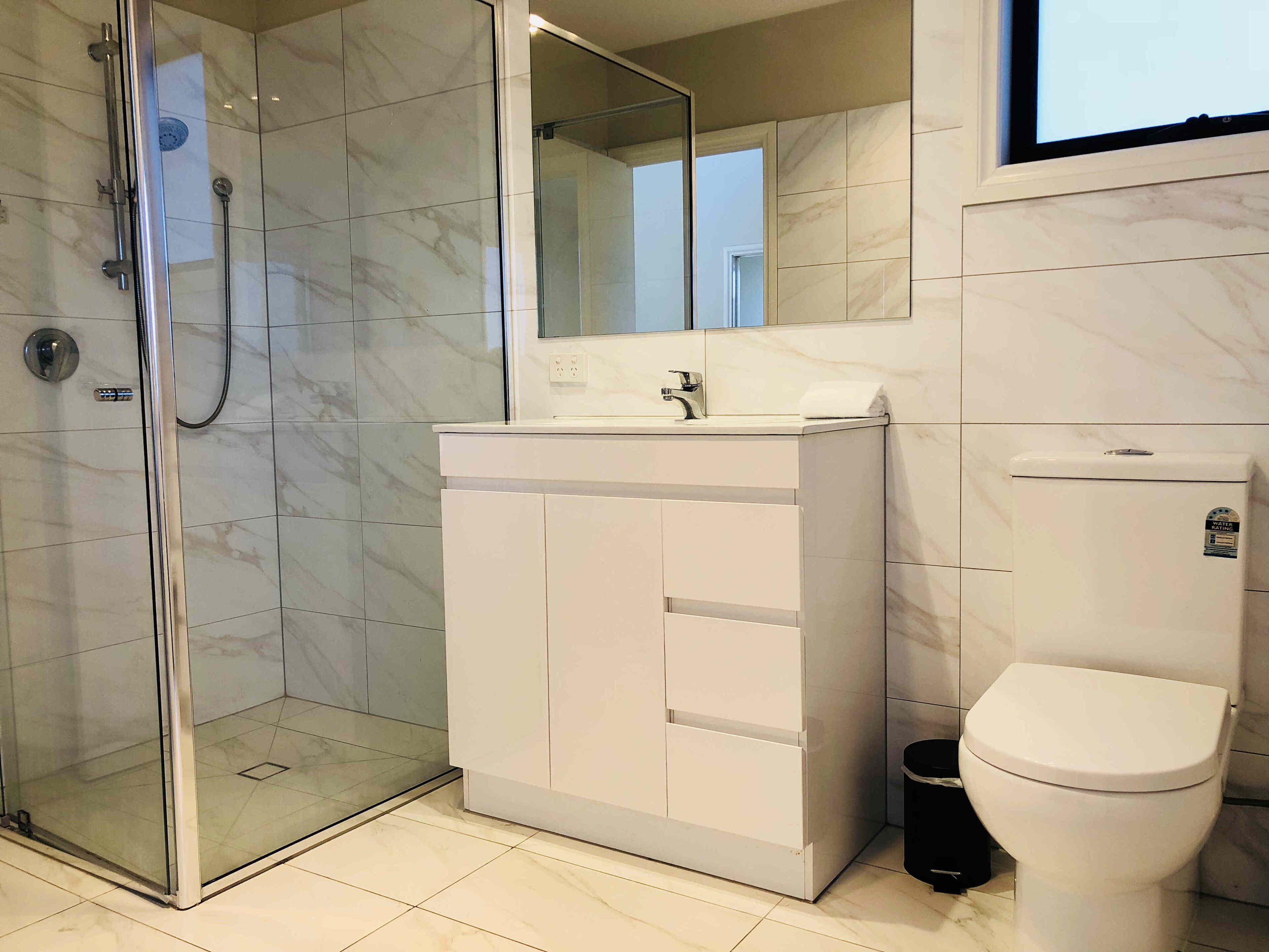Un baño moderno con ducha envuelta en vidrio, tocador blanco con espejo y un inodoro.