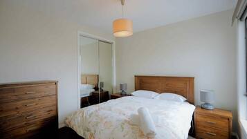 A bedroom with a wooden bed, a nightstand with a lamp, a dresser, and a mirror.