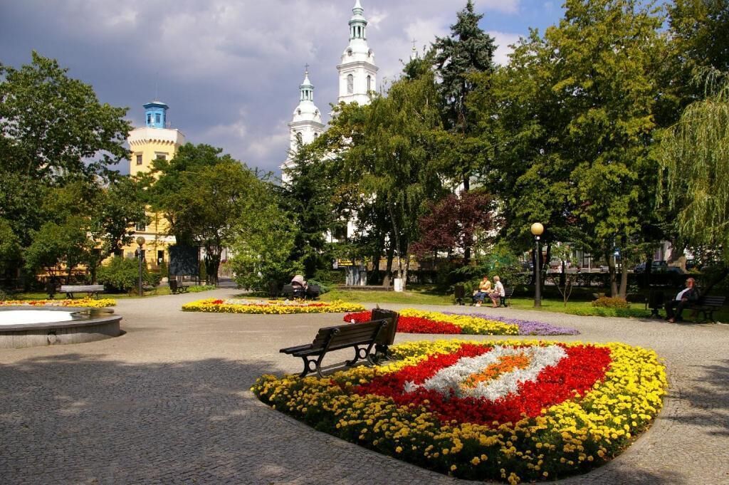 A park with flower beds, benches, and a distant view of a white building with towers.