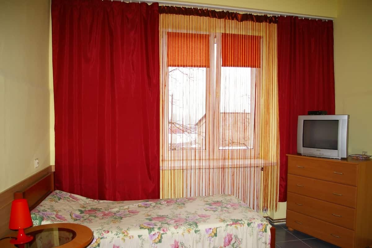 Una stanza con un letto, una televisione su una cassettiera in legno e una finestra con tende rosse.