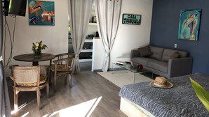 A modern living room with a sofa, a coffee table, a dining table with chairs, a TV, and artwork on the walls.