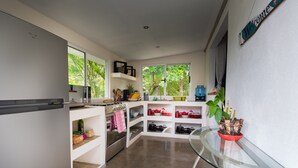 A modern kitchen with white cabinetry, a glass-top table, and a view of greenery outside.