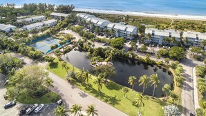 An aerial view of a resort with multiple buildings, a tennis court, a swimming pool, and a beach.