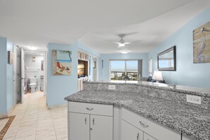 A modern kitchen with granite countertops, white cabinets, and a view to the outside.