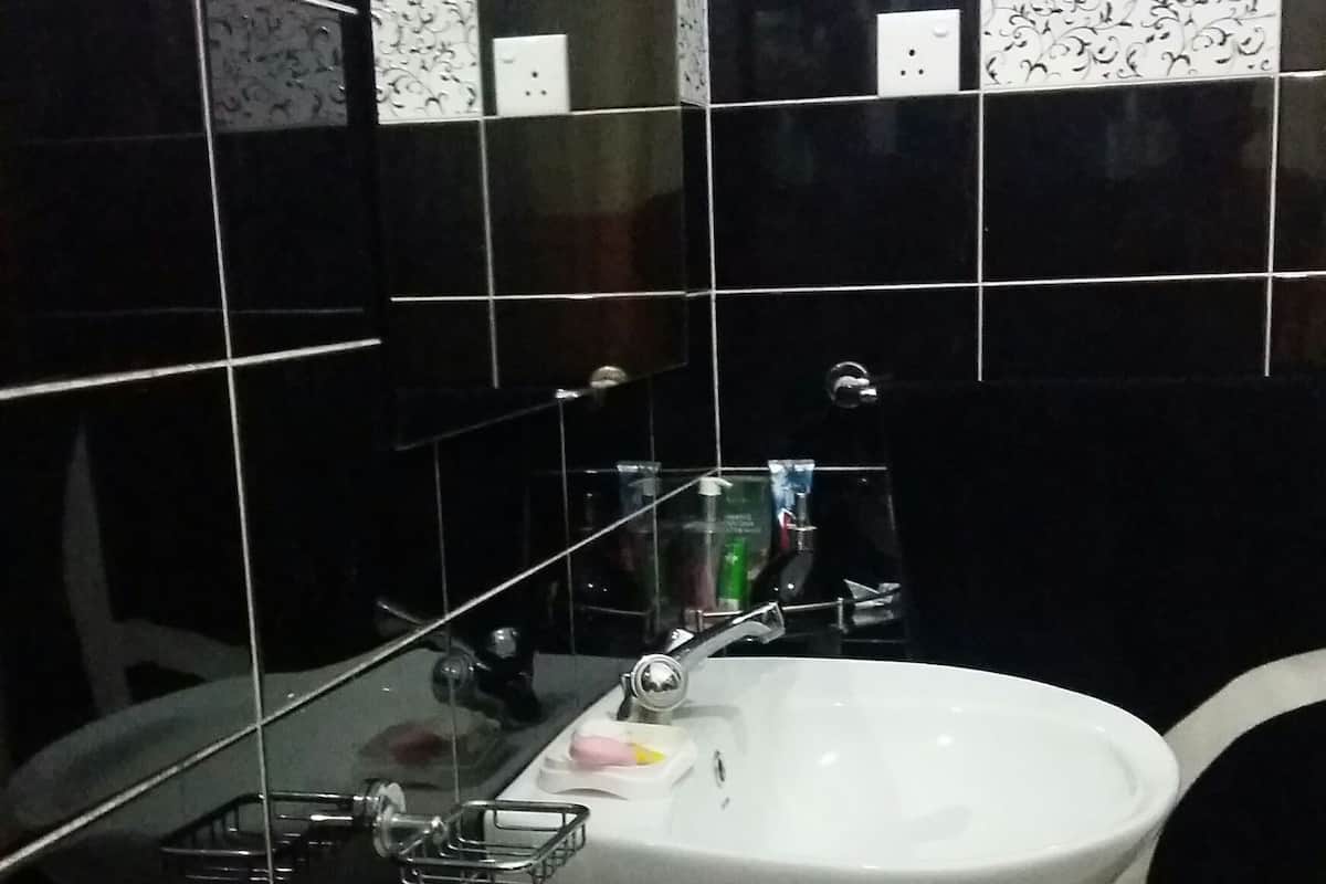 Ein Badezimmer mit einem weißen Waschbecken, schwarz-weißen Fliesen und einer Glasabtrennung.