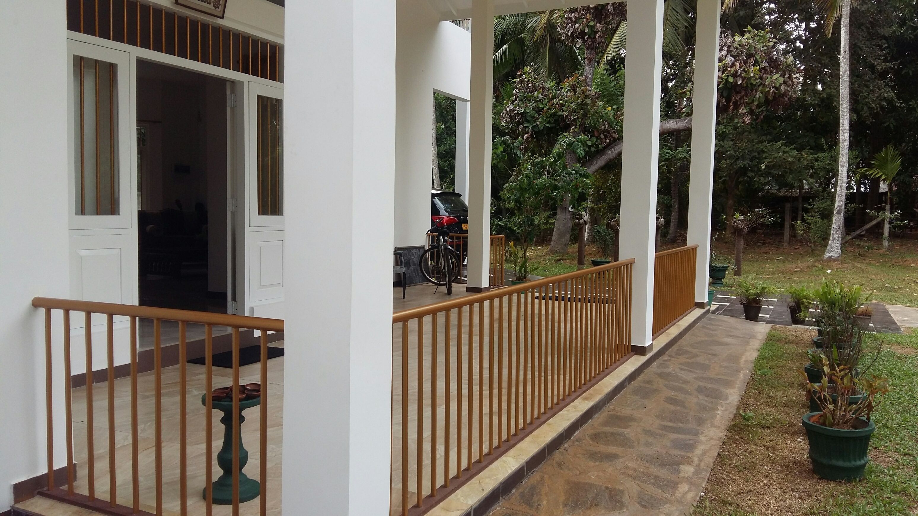A covered porch with a wooden railing, a bicycle, and a car parked outside.