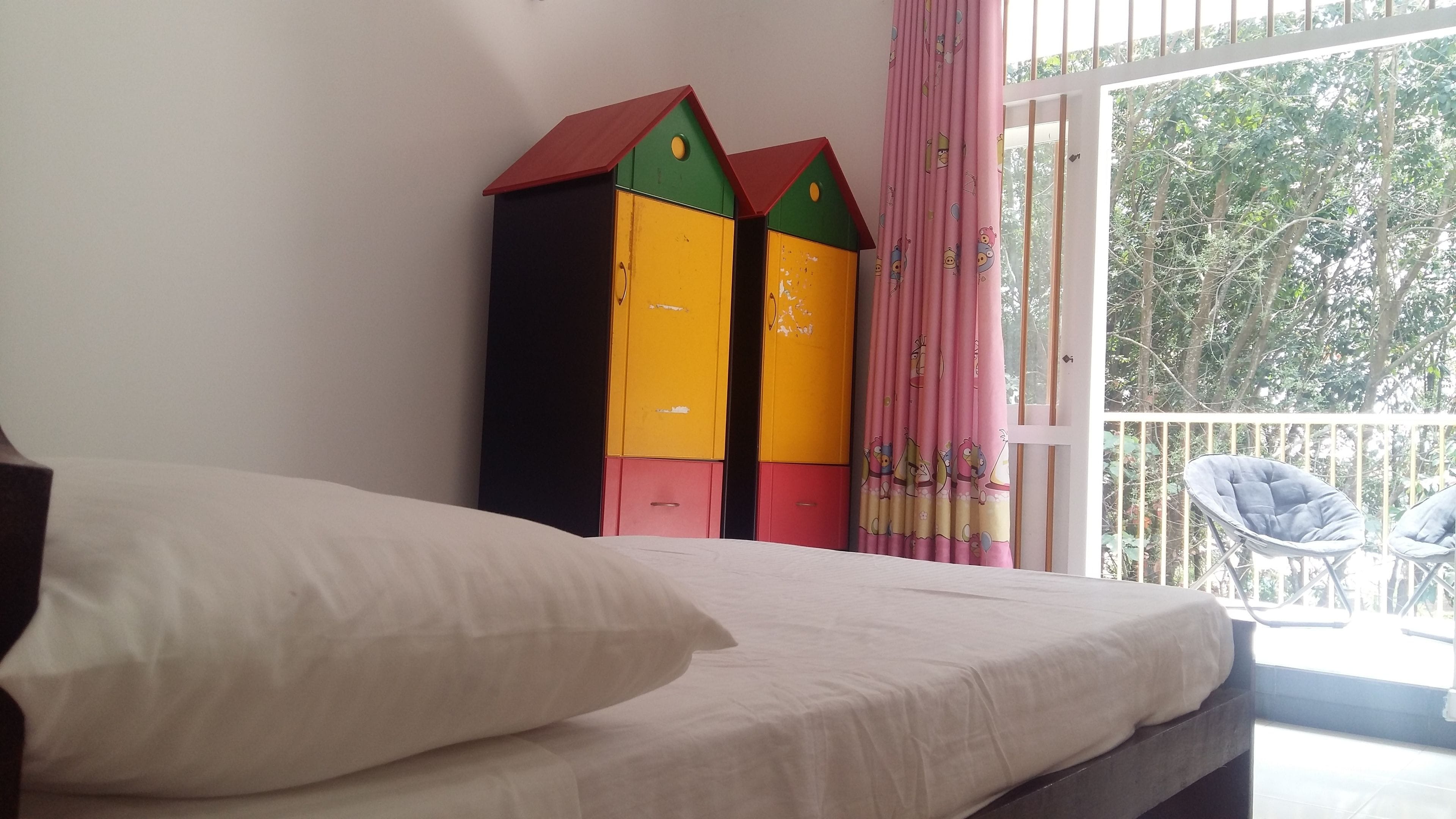 A bedroom with a bed, a window with curtains, and a balcony with chairs.