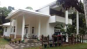 A two-story building with a covered porch, a car parked in front, and potted plants along the driveway. - White House (Ragama)