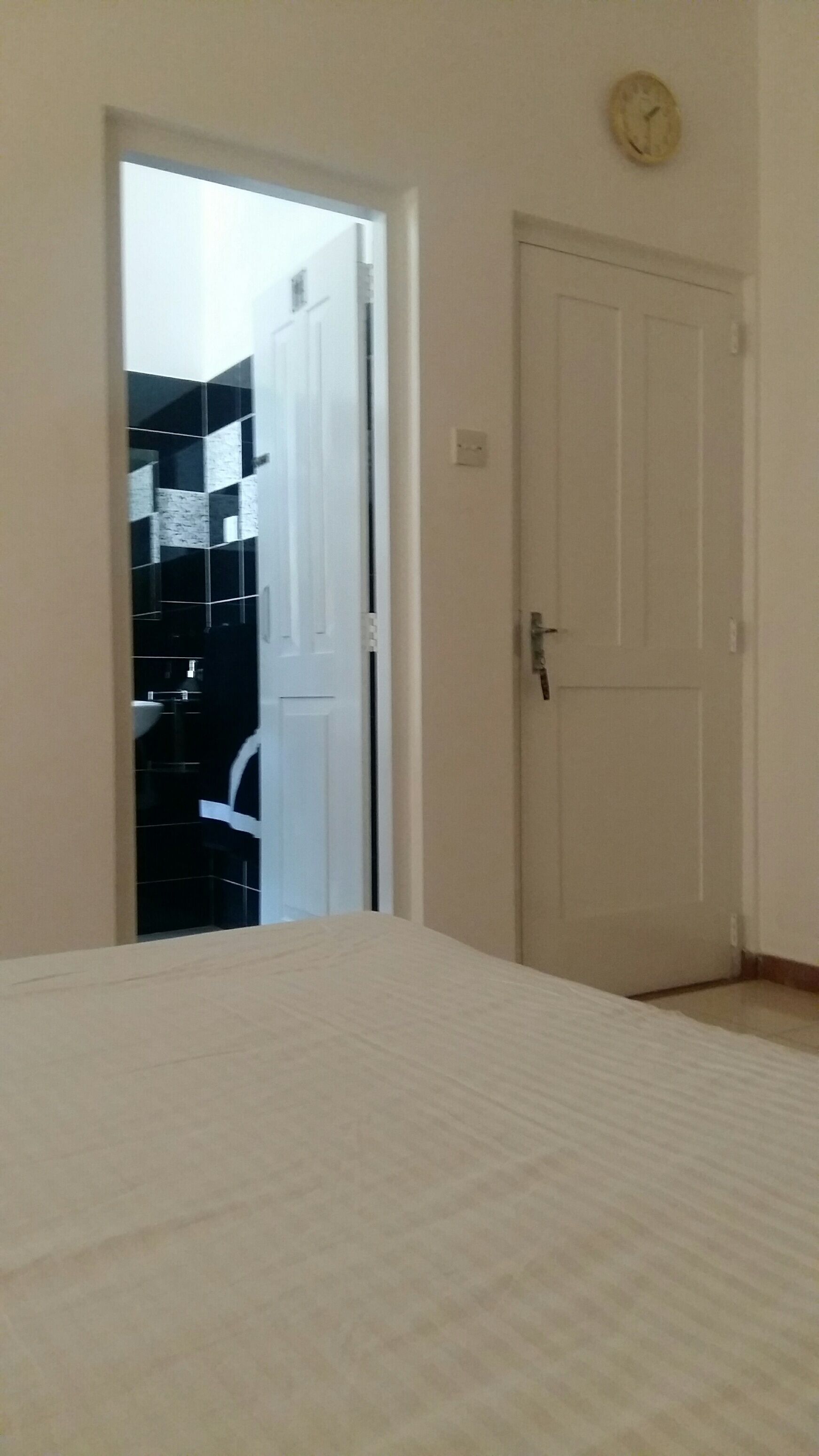 Una habitación con cama, puerta y vista al baño, que incluye un lavamanos y un espejo.