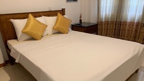 A neatly made bed with white and gold bedding, a wooden headboard, and a bedside table with a vase. - White House (Ragama)