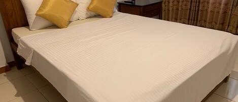 A neatly made bed with white and gold bedding, a wooden headboard, and a bedside table with a vase.