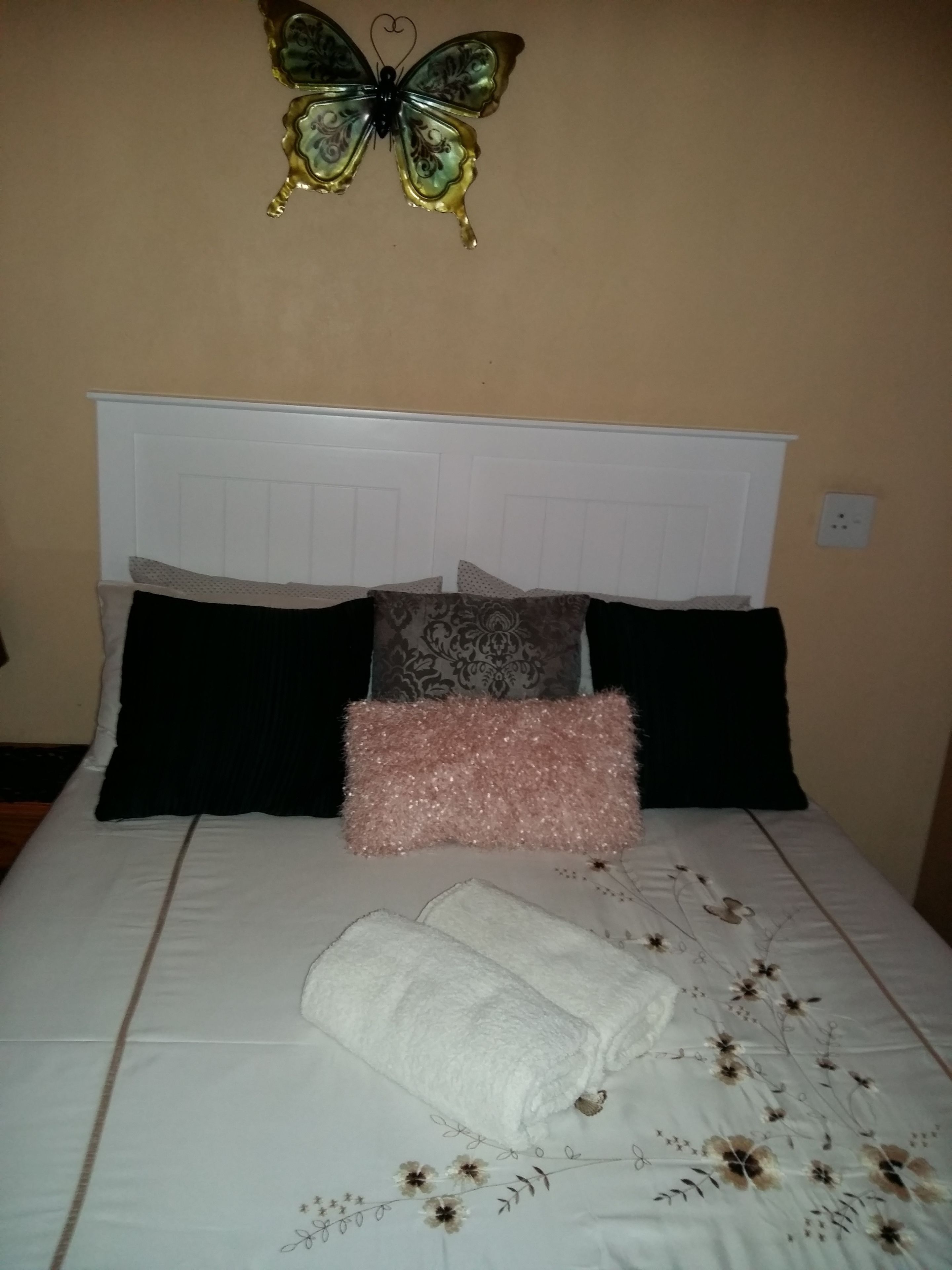 Uma cama bem arrumada com cabeceira branca, uma borboleta decorativa e um cobreleito estampado com flores.