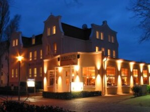 A building with a prominent sign reading "IMAGUSTA" at the entrance, featuring multiple windows and a well-lit facade. - Single room - Hotel Ostseestern (Kühlungsborn)