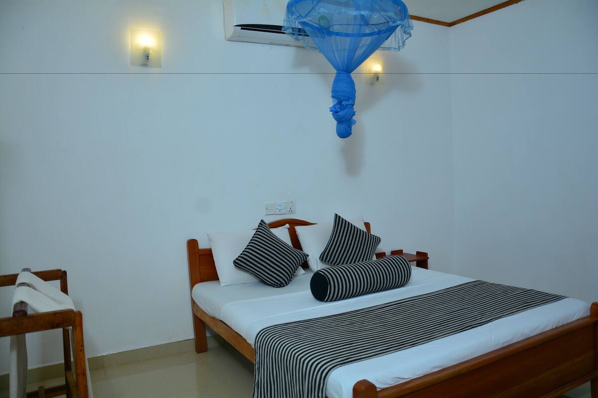 A bedroom with a wooden bed, white bedding, and a mosquito net hanging above.