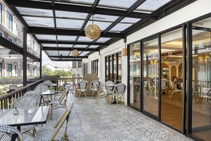 An outdoor patio with tables and chairs, a glass door leading inside, and a view of the street.