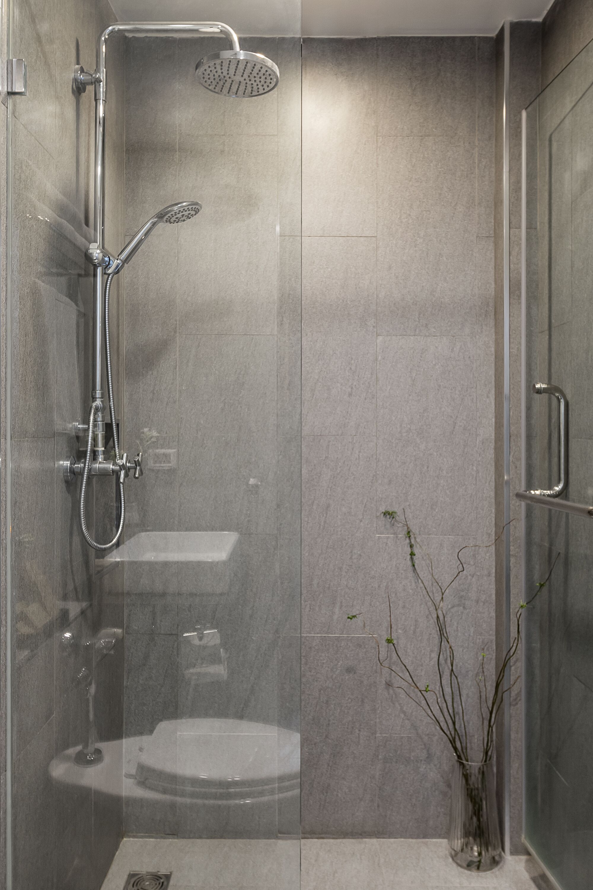 A modern shower enclosure with a glass door, a handheld showerhead, and a wall-mounted rain showerhead.