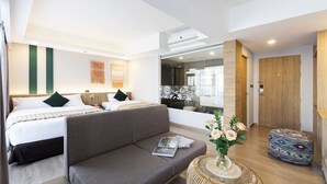 Une chambre d’hôtel moderne avec un grand lit, un canapé, une petite table ronde ornée d’un vase de fleurs et une porte en bois.