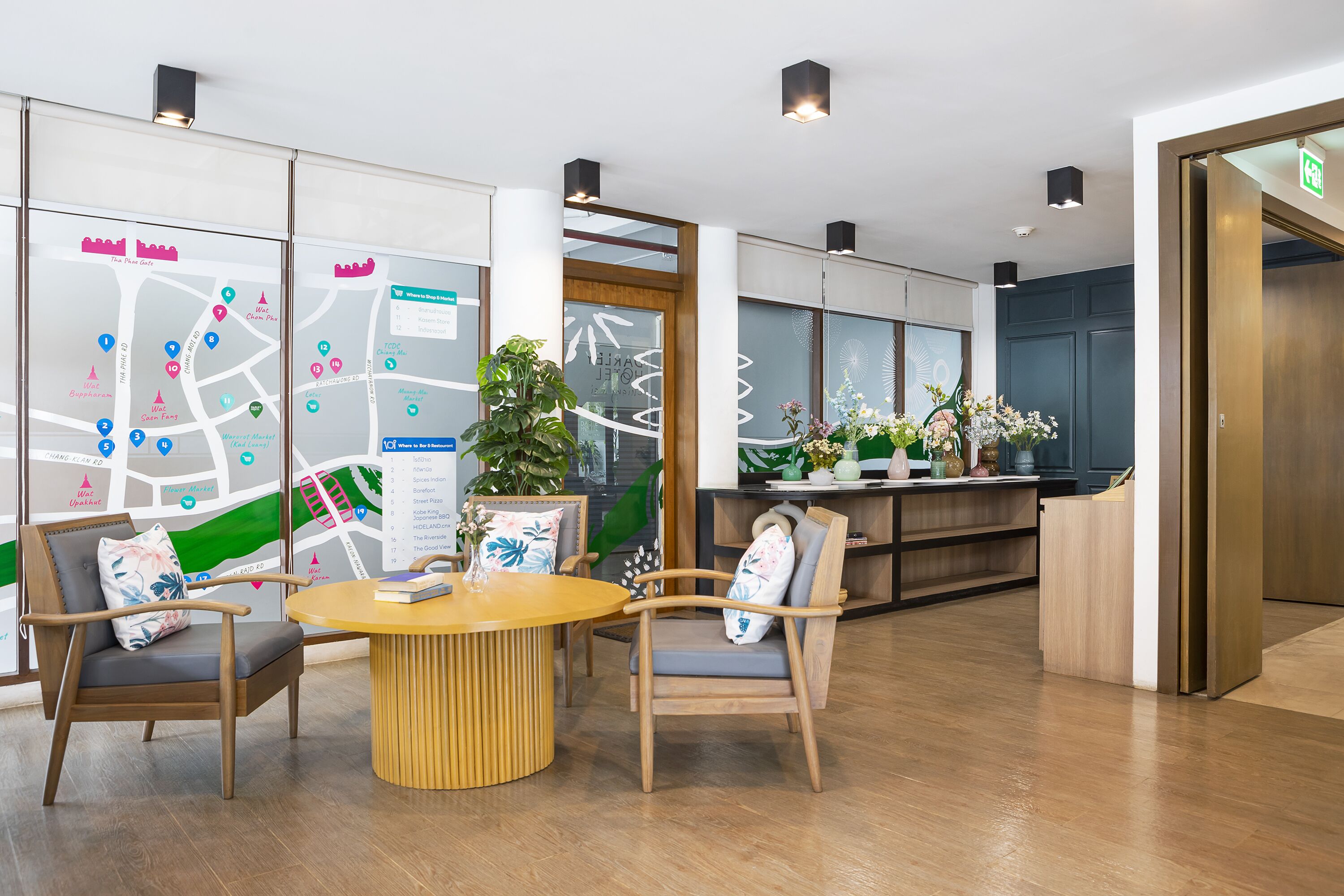 A modern reception area with a wooden reception desk, two wooden chairs with cushions, a round wooden table, and a large wall map.