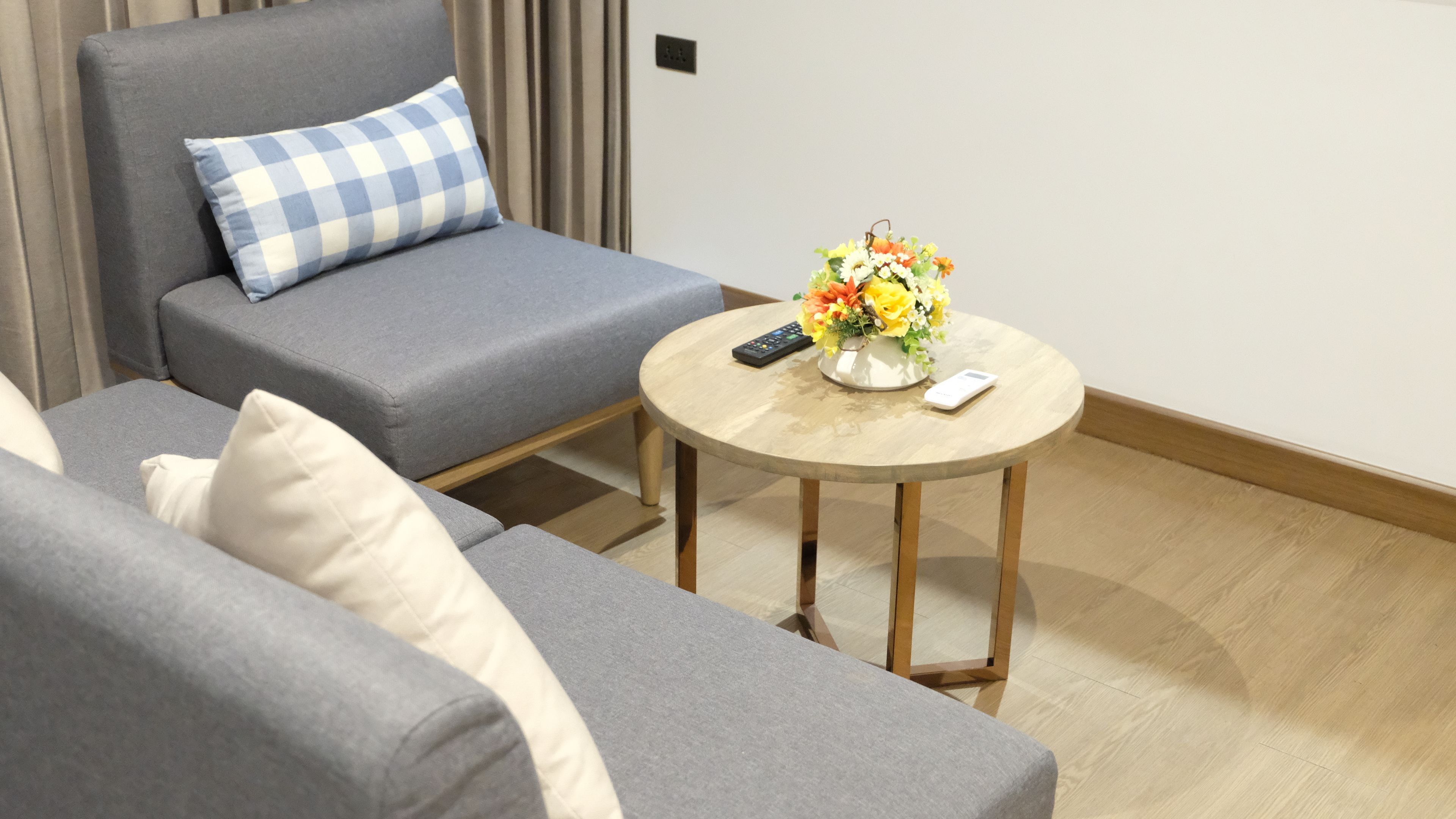 A modern living room with grey sofas, a round wooden coffee table, and a vase of flowers.