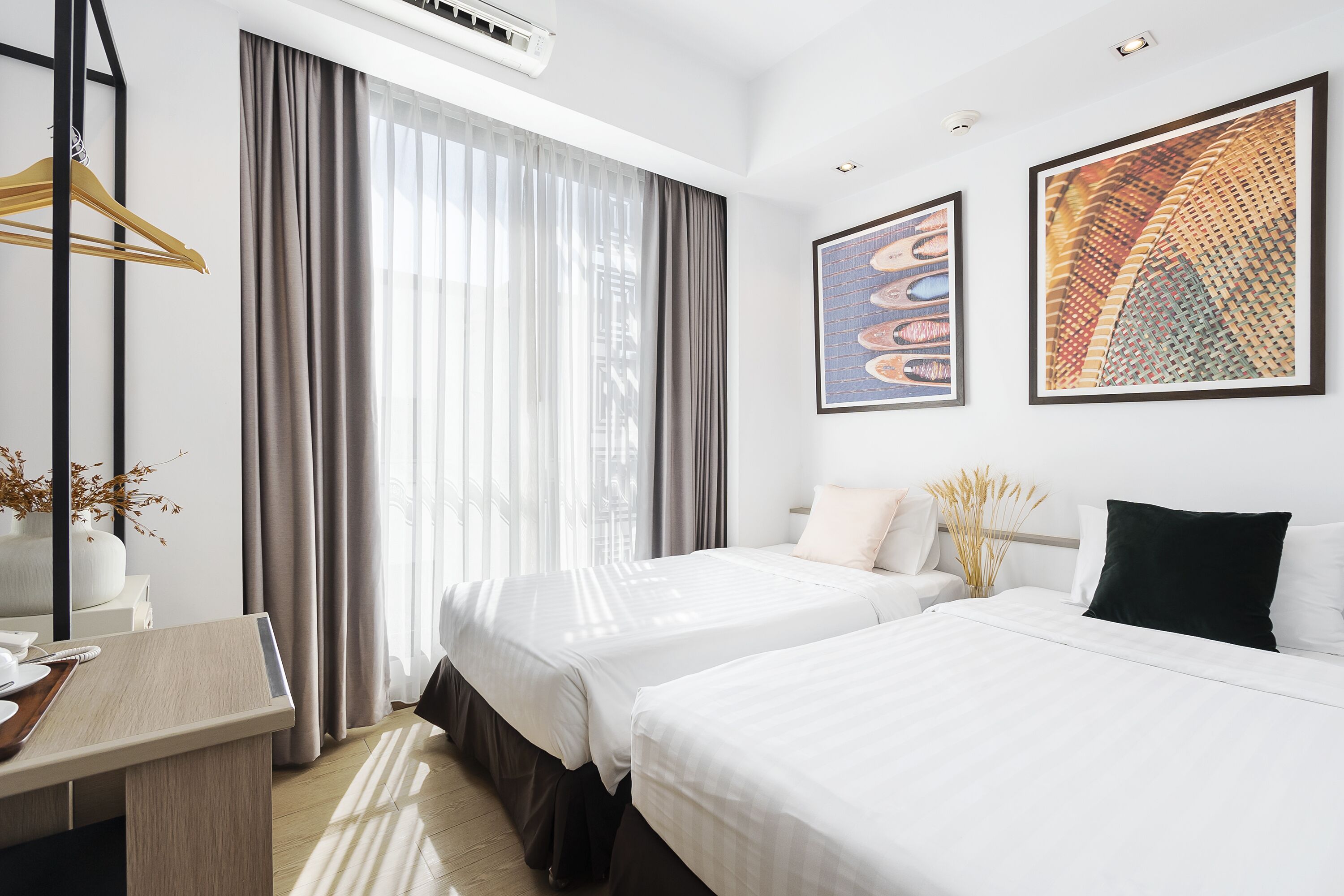 A hotel room with two beds, a desk, and a large window with curtains.