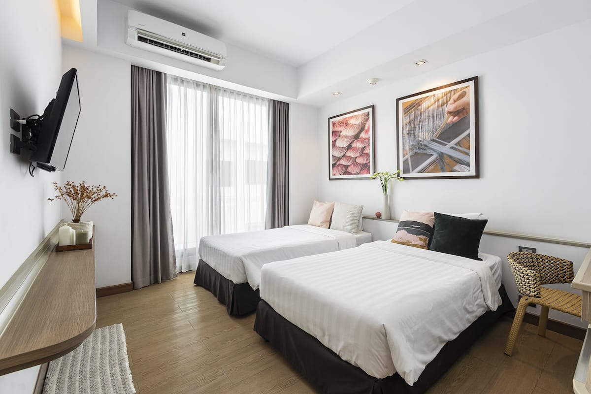 Habitación de hotel con dos camas, un escritorio, una silla y obras de arte en las paredes.