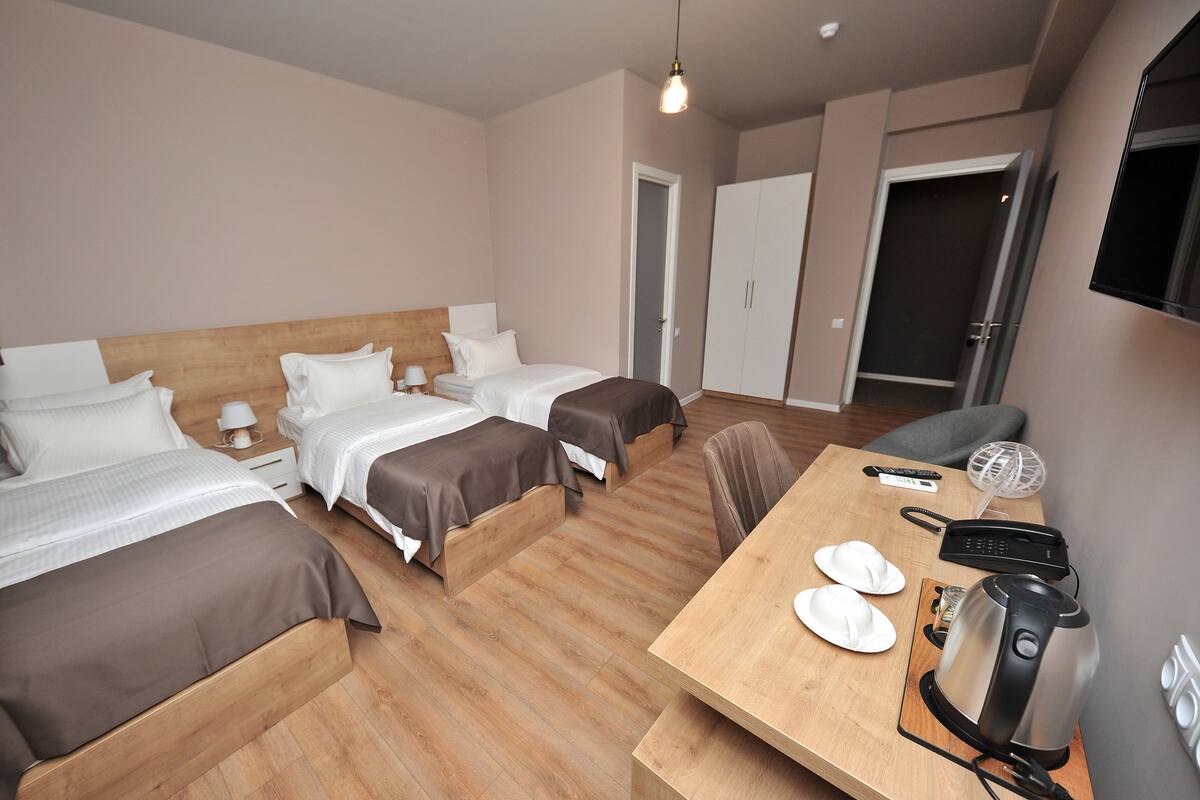 A hotel room with three beds, a wooden table with a coffee maker, and a TV mounted on the wall.