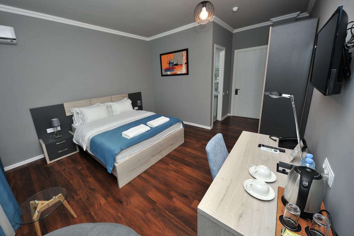 A hotel room with a bed, bedside tables, a desk with a coffee maker, a TV, and a painting on the wall.