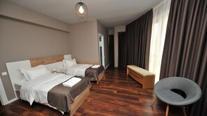 Une chambre d’hôtel moderne avec deux lits, une banquette, une chaise et une grande fenêtre avec des rideaux.