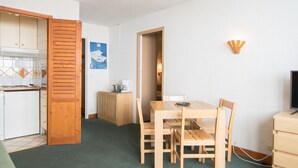 Een compacte kamer met een kitchenette, een eettafel met stoelen, een televisie en een klein kastje.