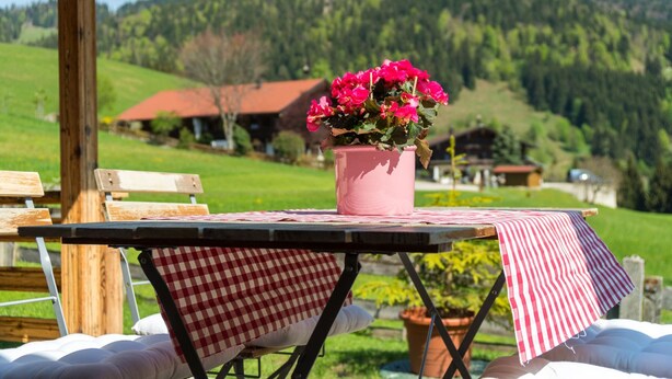 A table with a pink vase of flowers, a red and white checkered tablecloth, and a view of a mountain landscape in the background. - Alpenchalet Sachrang für 2 Personen (Sachrang)