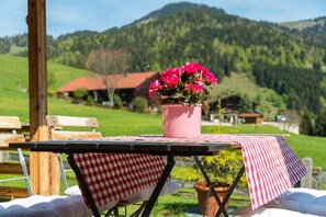 Una mesa con un jarrón rosa de flores, un mantel a cuadros rojo y blanco, y una vista de un paisaje montañoso al fondo.