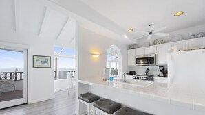 A modern kitchen with white cabinetry, a central island with bar stools, a microwave, and a ceiling fan. - H242: Modern 1BD Villa, Fantastic Ocean View, Fireplace, Golf Cart (Avalon)