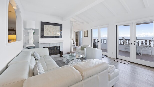 A spacious living room with a white sofa, a glass coffee table, and a fireplace. There is a balcony with a view of the sea. - H242: Modern 1BD Villa, Fantastic Ocean View, Fireplace, Golf Cart (Avalon)
