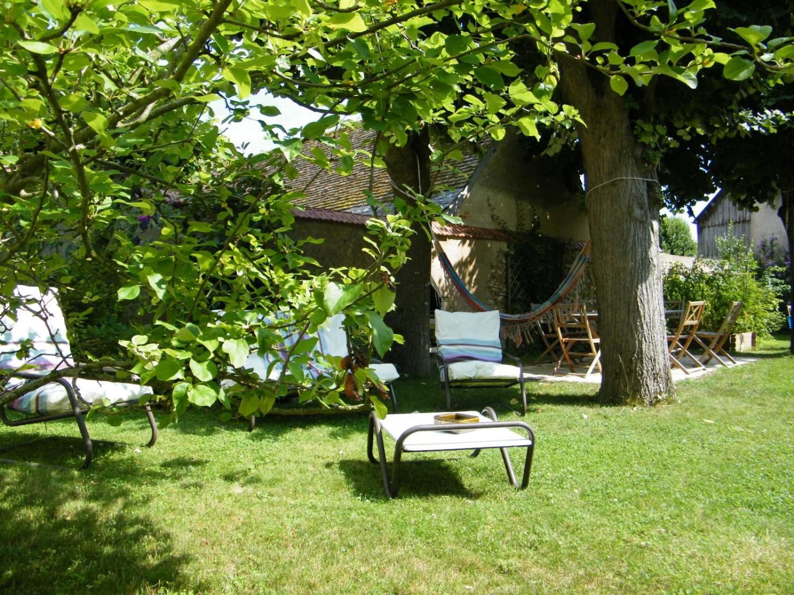 A garden with a hammock, a small table, and chairs under a tree.