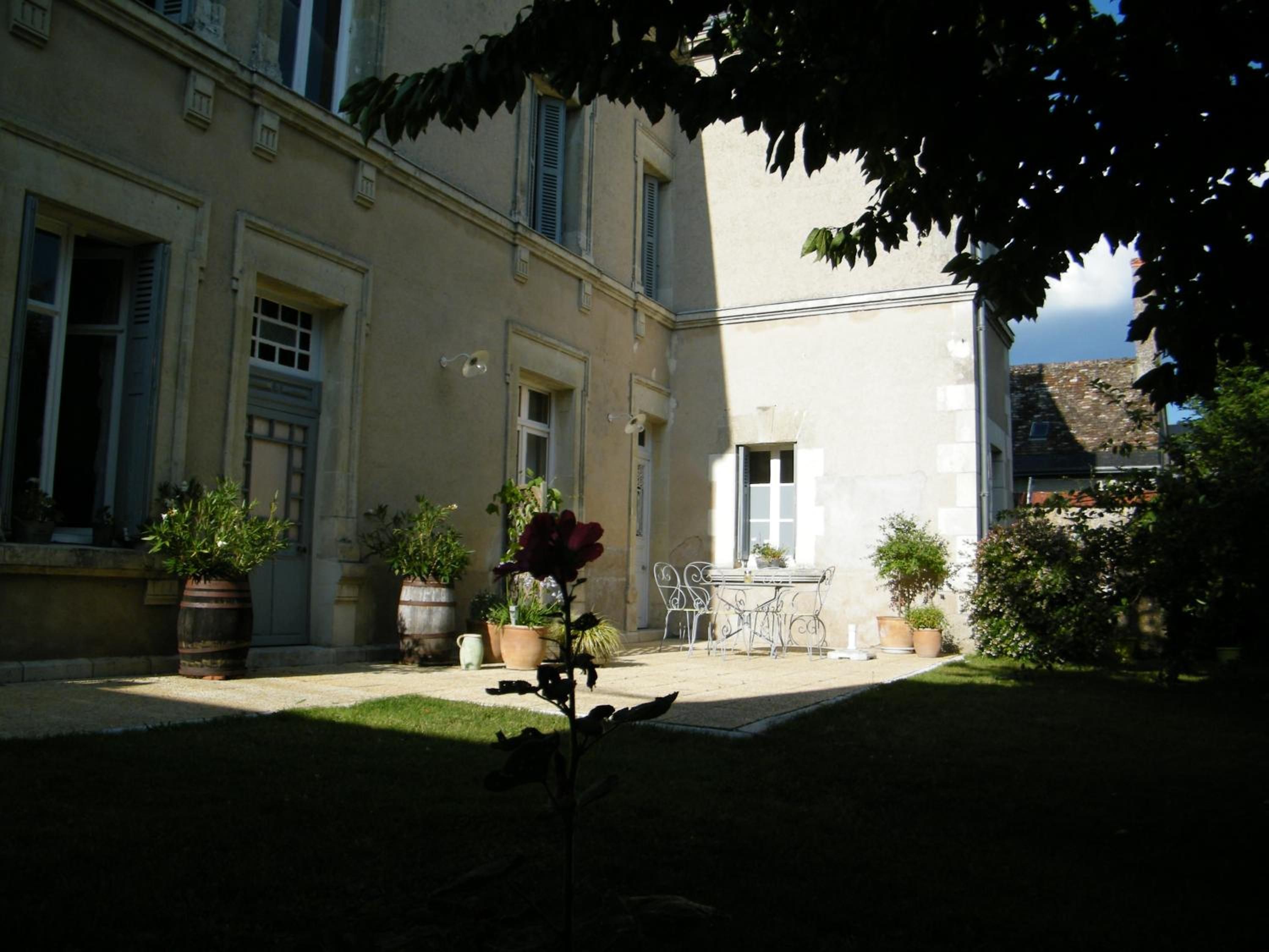 A courtyard with a table and chairs, potted plants, and a building with windows and shutters.