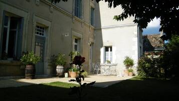 A courtyard with a table and chairs, potted plants, and a building with windows and shutters.