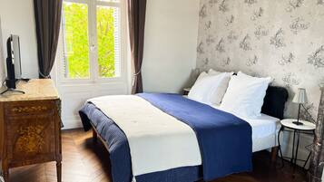 Een slaapkamer met een bed, een houten dressoir, een raam met gordijnen en een lamp.