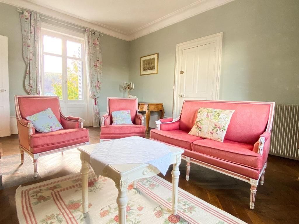 A room with a red sofa, two matching armchairs, a small table, and a window with curtains.