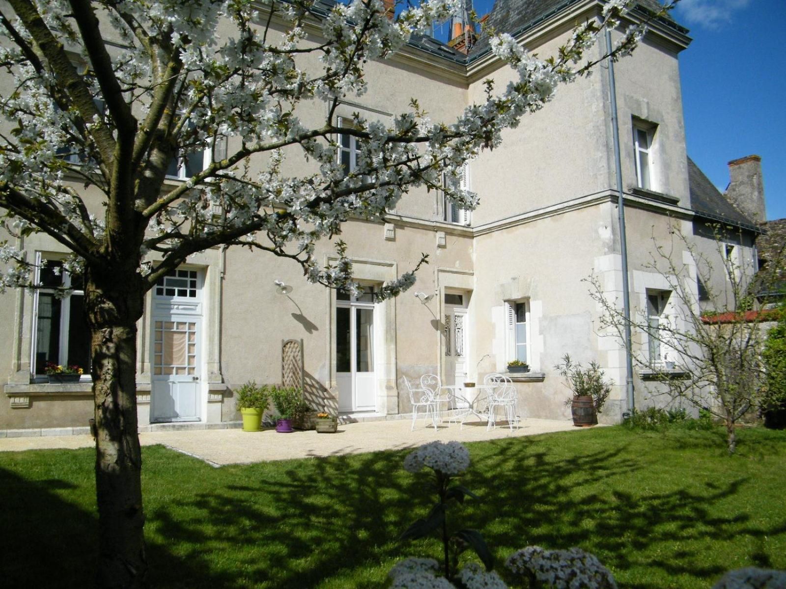 A two-story building with a garden area, outdoor seating, and a tree with white blossoms.