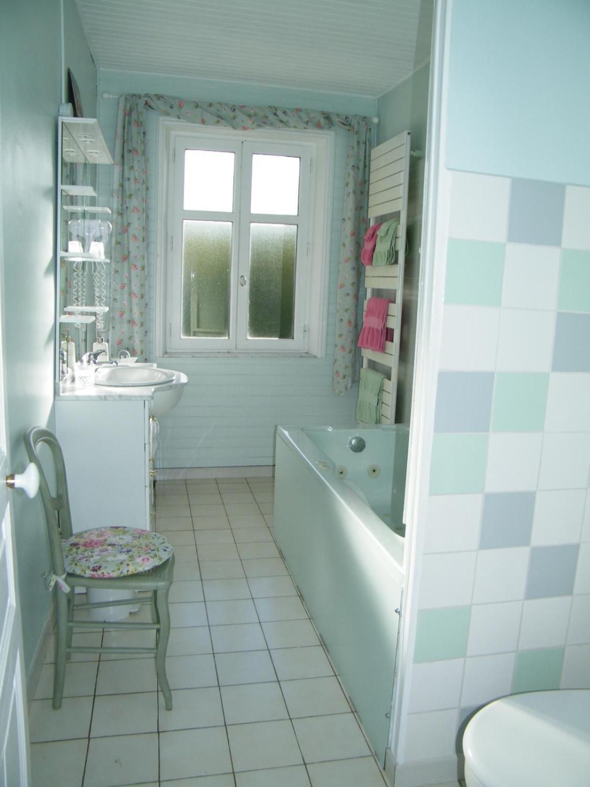 Un bagno con un water, un lavandino e una vasca. C'è una sedia con una seduta decorata con fiori e una finestra con tende floreali.