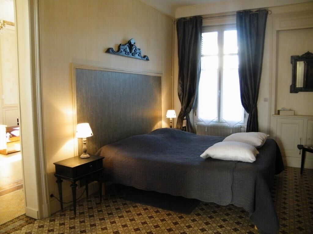 Une chambre d’hôtel avec un lit, deux lampes de chevet, une fenêtre avec des rideaux et un radiateur.