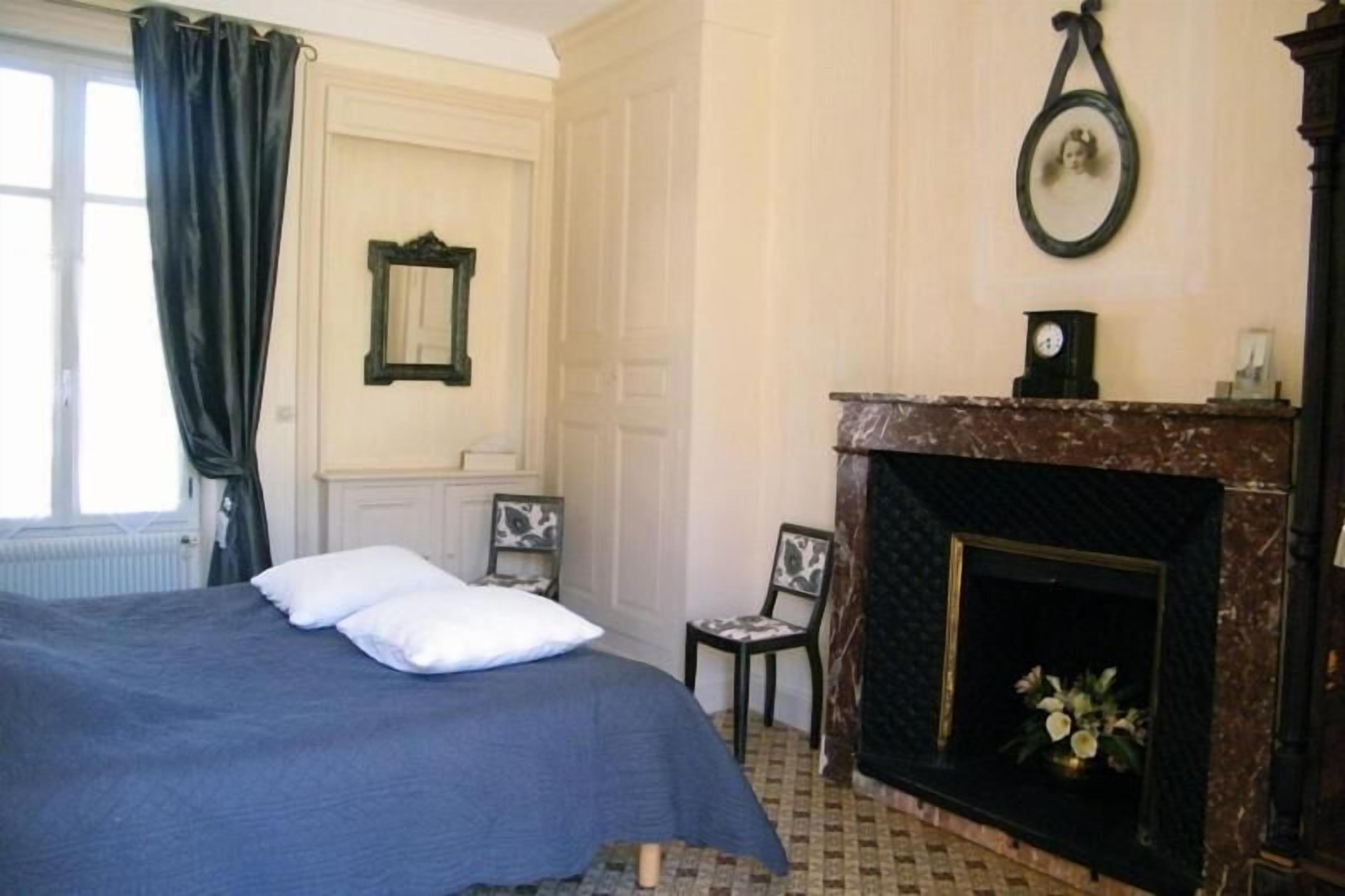A bedroom with a bed, a fireplace, a chair, and a window with curtains.