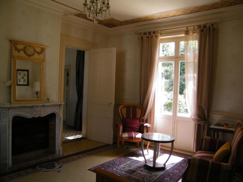 Una habitación con chimenea, una mesa, una silla y una ventana con cortinas.
